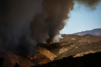 Flames race up the hill as the plume of smoke from the Hughes Fire fills the sky in Castaic, California