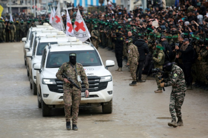 A Palestinian Hamas fighter precedes International Red Cross vehicles as they arrive in the central Gaza Strip to receive three Israeli hostages. Israeli Prime Minister Benjamin Netanyahu has described the described the ceremonies as "humiliating"